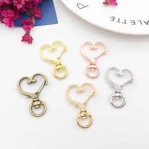 Puede incluir: Cuatro llaveros de metal en forma de corazón en diferentes acabados: dorado, oro rosa, plateado y latón antiguo. Cada llavero tiene un cierre giratorio y un anillo.