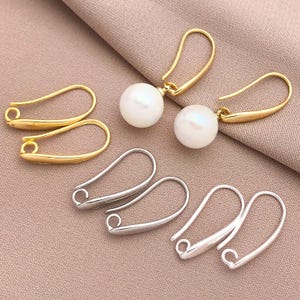 May include: Four pairs of earring findings, two gold and two silver. The gold findings have a pearl attached to the top. The silver findings are simple loops.