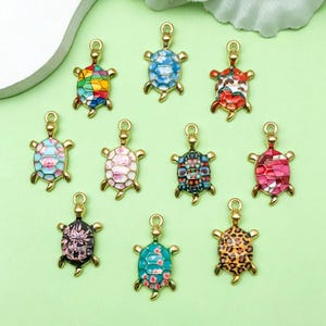 Può includere: Dieci ciondoli a forma di tartaruga dorati con diversi motivi in smalto colorato. I ciondoli sono perfetti per la creazione di gioielli, lo scrapbooking e altri progetti di artigianato.