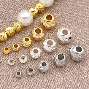 May include: A selection of gold and silver beads in different sizes. Some beads feature a textured, faceted pattern, while others are smooth. A strand of gold beads and a pearl bead are also present.