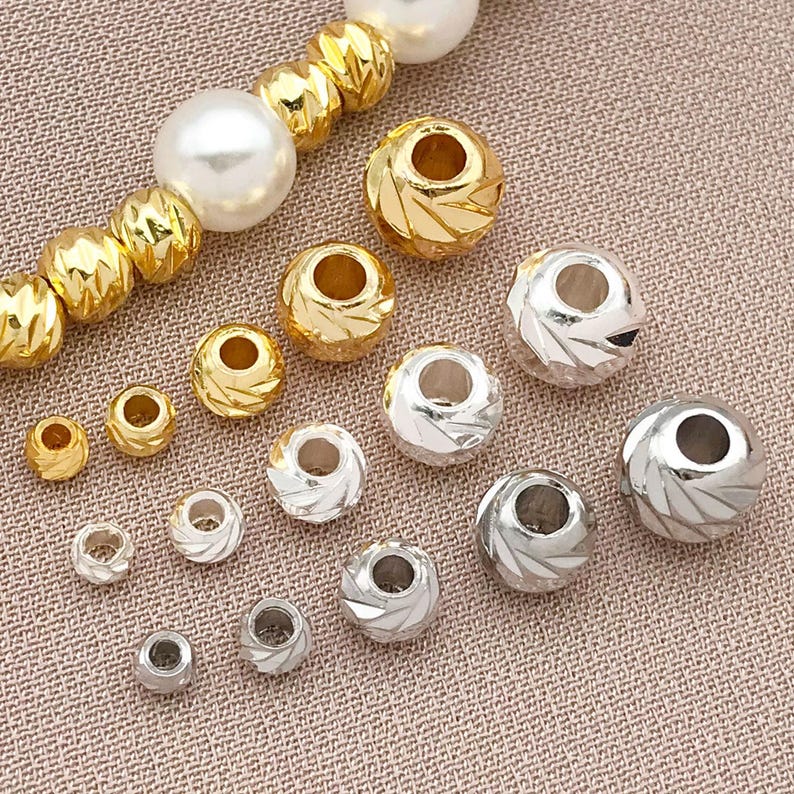 May include: A selection of gold and silver beads in different sizes. Some beads feature a textured, faceted pattern, while others are smooth. A strand of gold beads and a pearl bead are also present.