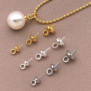 Puede incluir: Un collar dorado con un gran colgante de perla blanca y varios hallazgos de joyería dorados y plateados. Los hallazgos tienen un pequeño lazo y un poste. El fondo es de color neutro texturizado.
