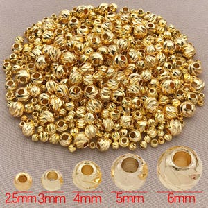 May include: A selection of gold-coloured metal beads, varying in size from 2.5mm to 6mm. The beads have textured surfaces, ideal for jewellery making and crafts. The image includes text indicating the bead sizes in millimetres.