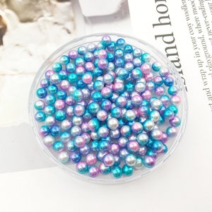 May include: A clear plastic container filled with iridescent blue and pink pearl beads.