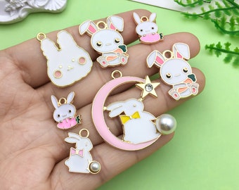 May include: A set of nine gold-tone metal charms featuring white bunny rabbits with pink and yellow accents. The charms include a crescent moon with a star, a bunny holding a carrot, and a bunny with a bow tie.