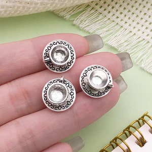 以下が含まれることがあります： ティーカップとソーサーの形をしたシルバーチャームペンダント3個。各ペンダントは、波状の縁と小さなハンドルが付いた詳細なデザインになっています。