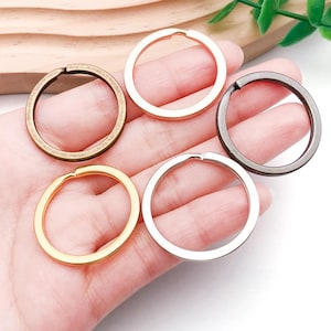 May include: Five metal key rings in various colors: gold, silver, bronze, rose gold, and gunmetal. Each ring is circular with a small opening for attaching keys or other items. The rings are held in a hand.
