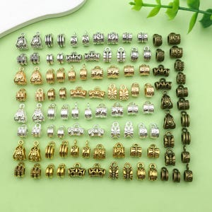 Op de afbeelding: Assortiment van metalen kralencaps in goud, zilver en brons. De caps hebben verschillende decoratieve ontwerpen en zijn ideaal voor het maken van sieraden.