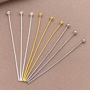 以下が含まれることがあります： シルバーとゴールドトーンのジュエリー用ヘッドピンの詰め合わせ。各ピンは上部に小さなボールと長いストレートワイヤーが付いています。ピンは、ジュエリー作りに最適な、質感のあるニュートラルカラーの表面に配置されています。
