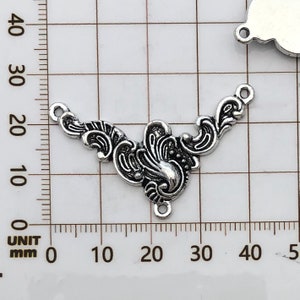 May include: Silver-toned metal connector with a decorative, ornate design. The connector has three loops for attaching jewelry or other crafts.