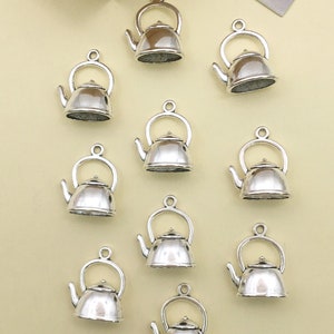 Może przedstawiać: Dziesięć srebrnych charmów w kształcie czajnika z pętelką do zawieszenia. Charmy są szczegółowo wykonane z dzióbkiem, uchwytem i pokrywką.