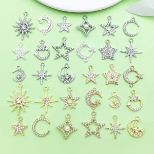 Puede incluir: Una colección de colgantes con temática celestial en tonos plateados y dorados. Los colgantes incluyen estrellas, lunas y diseños de sol, muchos incrustados con brillantes pedrería. Ideales para la creación de joyas y manualidades.