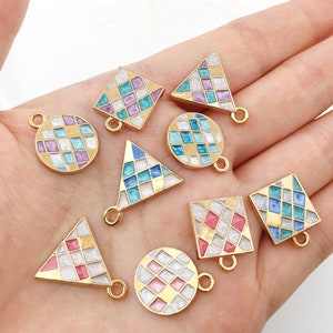 Könnte beinhalten: Sortiment an goldfarbenen Metall-Anhängern mit Emaille-Designs. Die Anhänger sind in Form von Kreisen, Quadraten und Dreiecken. Jeder Anhänger zeigt ein geometrisches Muster in Blautönen, Rosa und Weiß.