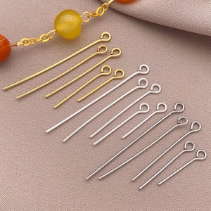 Puede incluir: Primer plano de un conjunto de alfileres de cabeza dorados y plateados con bucles. Los alfileres de cabeza están dispuestos en dos filas, con los alfileres dorados en la parte superior y los alfileres plateados en la parte inferior.