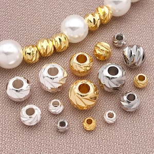 May include: A collection of gold and silver beads in different sizes and styles. Some have a textured, cut appearance, while others are smooth. A strand of large, white pearl beads is also present.