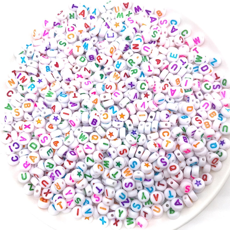 May include: A large pile of white plastic alphabet beads with colorful letters and star accents.