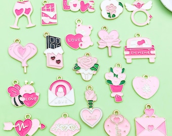 May include: A collection of pink enamel charms with gold-colored accents. The charms include hearts, roses, a teddy bear, a car, and the word "LOVE". The charms are designed for jewelry making or crafting.