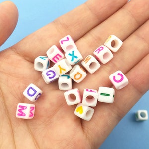 May include: A collection of white plastic letter beads with colorful letters. The beads have a hole in the center and are perfect for crafting.