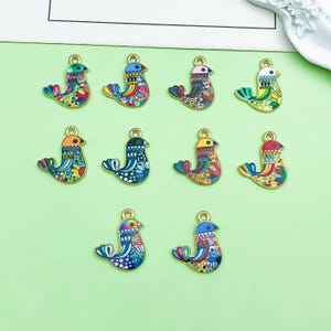 May include: Ten metal bird charms arranged in three rows, each featuring a unique colorful enamel pattern with intricate geometric and floral details. Every charm includes a small gold-toned loop at the top for attachment, showcasing vibrant hues.