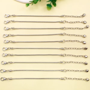 Puede incluir: Diez pulseras de cadena de serpiente plateadas con cierres en forma de corazón. Cada pulsera tiene una pequeña extensión de cadena con un dije en forma de corazón.