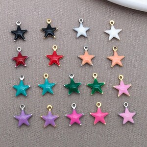 May include: A collection of star-shaped charms in various colors, including black, white, red, coral, teal, green, purple, and pink. Each charm has a silver or gold-colored loop for attaching to jewelry or crafts. The charms are arranged on a neutral background.