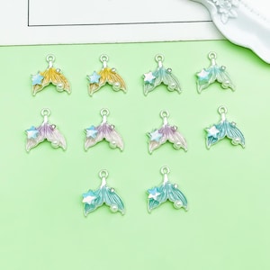 May include: Ten silver-toned metal charms shaped like mermaid tails, each featuring a small iridescent star and a white faux pearl accent. The charms are finished with enamel in various pastel colors including yellow, purple, blue, and green.