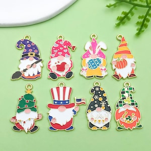 May include: Set of ten colorful enamel gnome charms with different designs, including a gnome with a pumpkin, a gnome with a heart, a gnome with a Christmas tree, and a gnome with an American flag. The charms are made of metal and have a gold finish.