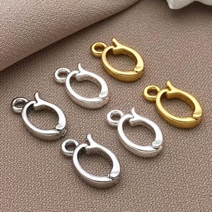 Peut inclure: Six fermoirs de bijoux ovales en or et argent. Les fermoirs ont une petite boucle à une extrémité et une fermeture à charnière à l'autre. Les fermoirs sont disposés sur un tissu de couleur neutre.