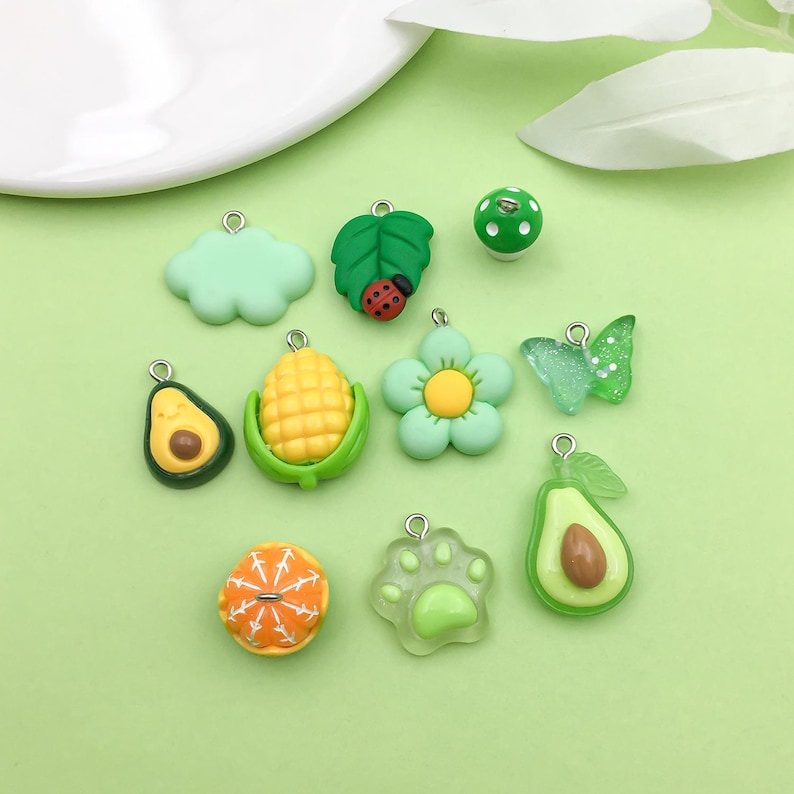 Puede incluir: Surtido de 10 dijes de resina verde y amarilla con anillos de salto plateados. Los dijes incluyen una nube, una hoja, una mariquita, ma&iacute;z, una flor, una mariposa, un aguacate, una huella de pata, una naranja y un hongo.