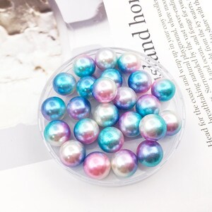 May include: A close-up of a clear container filled with iridescent blue, pink, and white pearl beads.