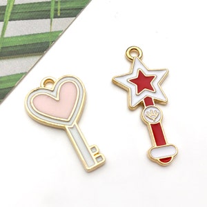 May include: Two gold-tone key charms, one shaped like a heart with a pink center and the other shaped like a star with a red center.