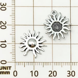 K&ouml;nnte beinhalten: Zwei silberfarbene Sonnenanh&auml;nger. Jeder Anh&auml;nger hat ein zentrales kreisf&ouml;rmiges Design mit strahlenf&ouml;rmigen Strahlen. Ein Anh&auml;nger hat eine Schlaufe zur Befestigung. Die Anh&auml;nger werden vor einem Rasterhintergrund mit Millimeterma&szlig;en angezeigt.