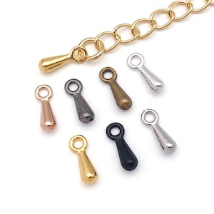May include: A collection of small, teardrop-shaped jewelry charms in various metallic finishes, including gold, silver, and bronze. A gold-colored chain is also visible. These charms are likely used for jewelry making or crafting.