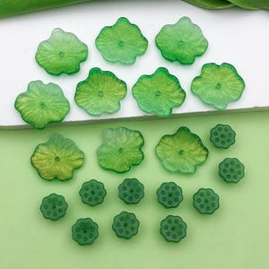Könnte beinhalten: Eine Sammlung grüner und weißer Harz-Knöpfe in Form von Lotusblumen und Lotuskapseln. Die Knöpfe sind in verschiedenen Größen und haben eine glänzende Oberfläche.