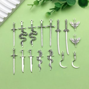 Puede incluir: Una colección de 14 dijes de metal plateados con varios diseños, incluyendo espadas, serpientes, mariposas y lunas crecientes. Estos dijes son perfectos para la elaboración de joyas, el scrapbooking y otros proyectos de manualidades.