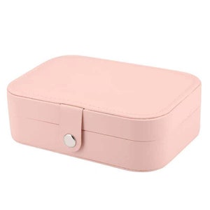 May include: A pink faux leather jewellery box with a silver button closure. The box has two compartments for storing jewellery.