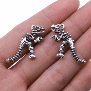 May include: A pair of silver dinosaur skeleton earrings. The earrings are small and detailed, with a realistic skeletal design.