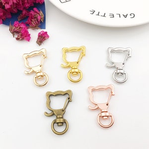 May include: Five metal cat-shaped keyrings in different colours: gold, silver, bronze, rose gold, and black. Each keyring has a swivel hook and a ring.