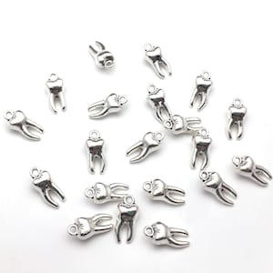Op de afbeelding: Een strooisel van zilveren tandcharms, elk met een kleine lus om te bevestigen aan sieraden of andere knutselwerkjes.