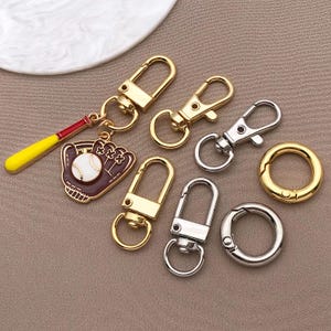 May include: A set of seven gold and silver keychains. The keychains feature a variety of designs, including a baseball glove, a baseball, and a simple loop. The keychains are perfect for adding a touch of personality to your keys.