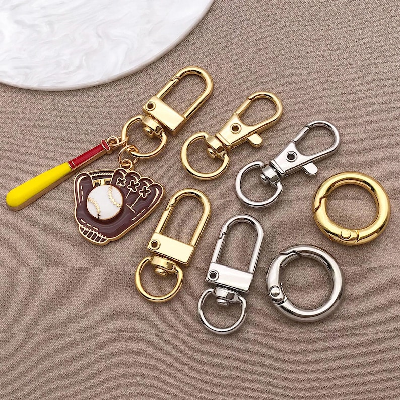 May include: A set of seven gold and silver keychains. The keychains feature a variety of designs, including a baseball glove, a baseball, and a simple loop. The keychains are perfect for adding a touch of personality to your keys.