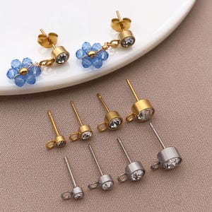 May include: Gold and silver stud earrings with clear crystal details. Two pairs have blue beaded flower drops. The earrings are shown on a white plate and a neutral surface. The earrings are suitable for pierced ears.