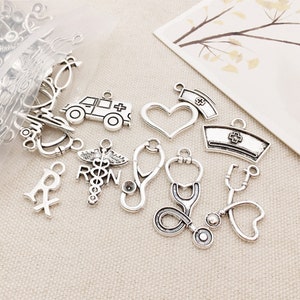 May include: A collection of silver-toned metal charms with medical themes, including a stethoscope, a heart, a cross, a pill bottle, an ambulance, and a nurse's cap.