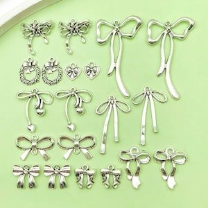 Op de afbeelding: Een verzameling zilverkleurige metalen bedels met verschillende strikdesigns. De bedels zijn perfect voor het maken van sieraden, scrapbooking en andere knutselprojecten.