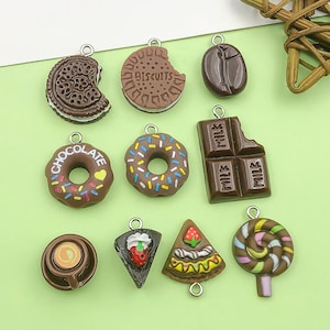 May include: A collection of brown food-themed charms, including a donut with sprinkles, a chocolate bar, a coffee cup, a cookie, a slice of cake, a lollipop, a coffee bean, and a biscuit. Each charm has a silver loop for attaching to jewelry or crafts.