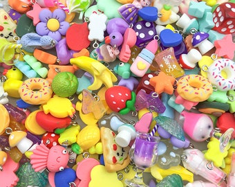 Può includere: Una grande collezione di ciondoli colorati in plastica con varie forme e design, tra cui ciambelle, fragole, funghi e un bicchiere di succo viola. I ciondoli hanno anelli a salto argentati per essere attaccati a gioielli o altri oggetti artigianali.