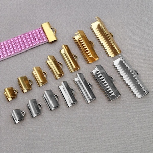 Può includere: Un assortimento di terminali a crimpare in metallo dorato e argentato, con un cinturino rosa tempestato di strass. I terminali variano per dimensioni e design, con bordi lisci e seghettati e piccoli anelli.