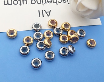 May include: A collection of silver and gold metal beads with a clear centre. The beads are round and have a hole in the centre.