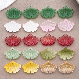 May include: A collection of twenty ginkgo leaf-shaped charms arranged in five rows of four. The charms feature a variety of translucent and opaque colours including green, white, pink, red, light green, olive, yellow, and beige, each with a small hole.