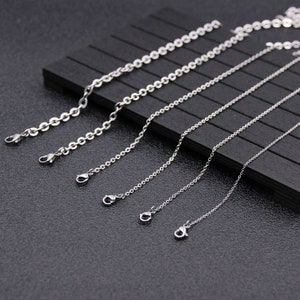 May include: Five silver chains of varying lengths, each with a lobster clasp closure. The chains are arranged in order of length, with the shortest chain at the top and the longest chain at the bottom.